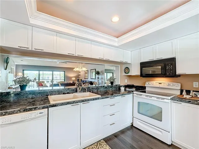 Kitchen featuring dark hardwood / wood-style floors, a tray ceiling, crown molding, white cabinets, and white appliances
