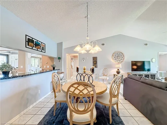 Tiled dining area with vaulted ceiling, a textured ceiling, and a chandelier