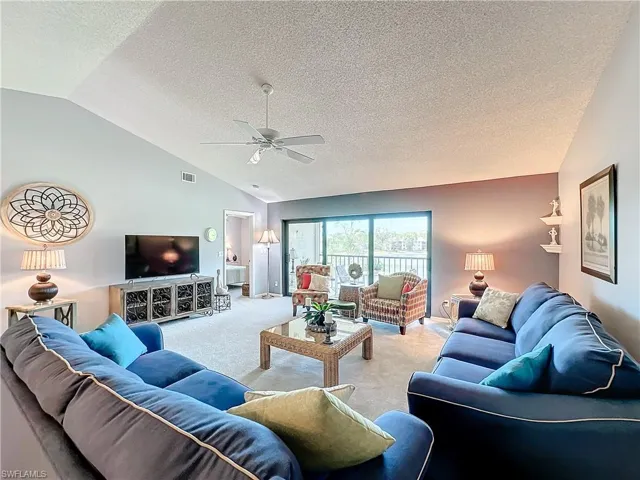 Carpeted living room with ceiling fan, a textured ceiling, and lofted ceiling