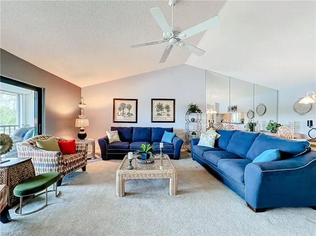 Living room featuring carpet, ceiling fan, a textured ceiling, and lofted ceiling