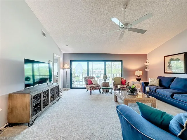 Carpeted living room with vaulted ceiling, ceiling fan, and a textured ceiling