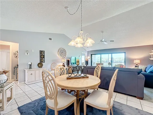 Tiled dining room featuring ceiling fan with notable chandelier, vaulted ceiling, and a textured ceiling