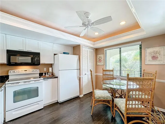 Kitchen with dark hardwood / wood-style flooring, ceiling fan, a tray ceiling, white cabinetry, and white appliances