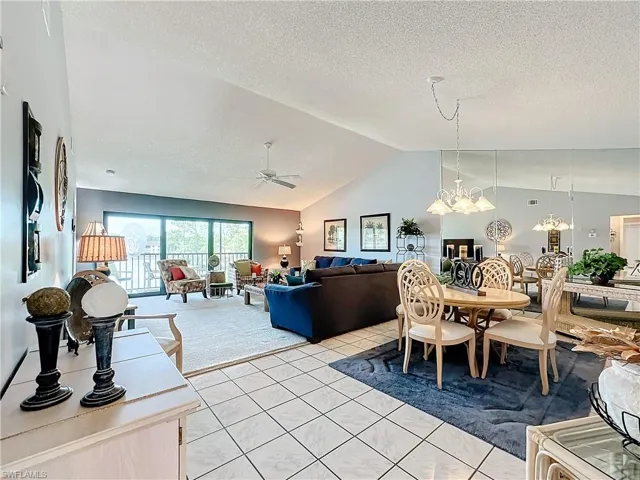 Dining space with high vaulted ceiling, a textured ceiling, light tile floors, and ceiling fan with notable chandelier