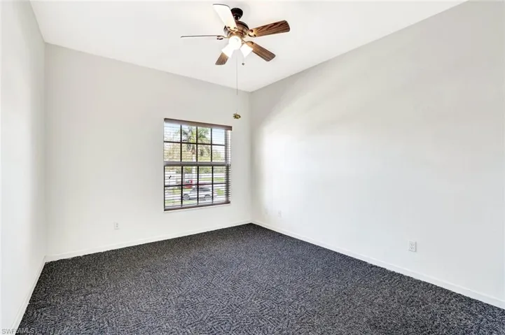 Empty room featuring dark colored carpet, a ceiling fan, and baseboards