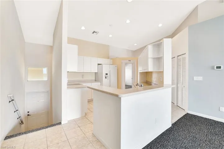 Kitchen featuring white refrigerator with ice dispenser, visible vents, light countertops, open shelves, and light tile patterned flooring