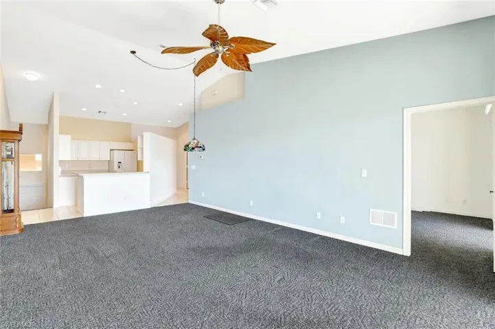 Unfurnished living room featuring a ceiling fan, visible vents, light carpet, and baseboards