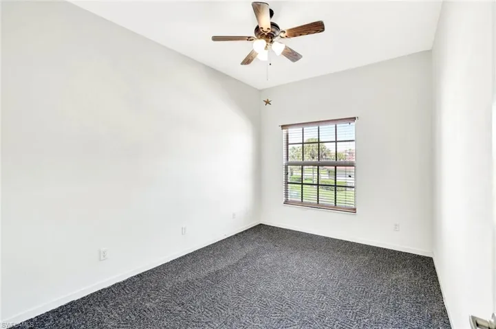 Spare room featuring ceiling fan, dark colored carpet, and baseboards