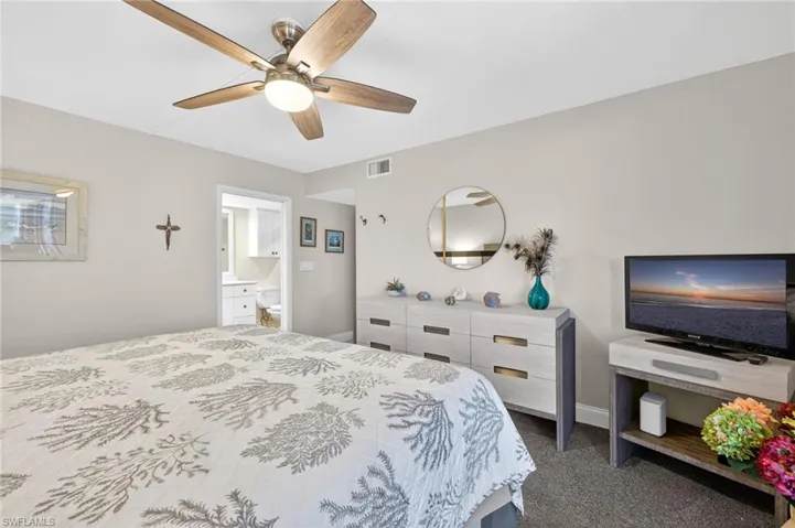 Bedroom with dark carpet, ceiling fan, and ensuite bath