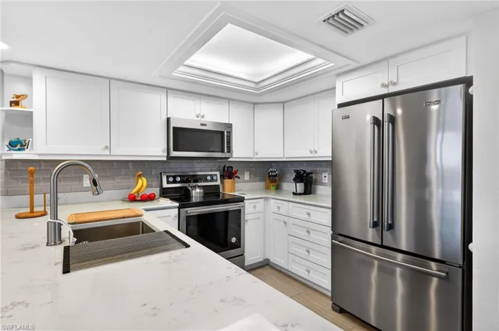 Kitchen with stainless steel appliances, white cabinetry, and light stone countertops