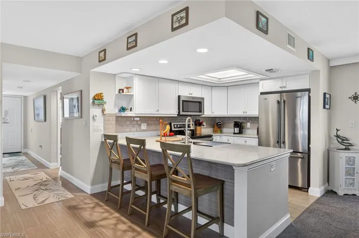 Kitchen featuring open shelves, stainless steel appliances, a peninsula, white cabinetry, and light stone countertops