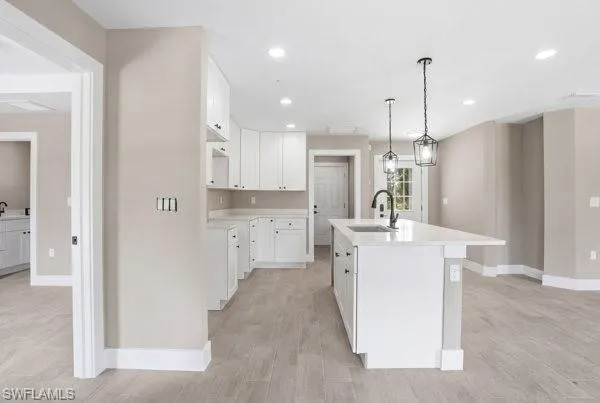Kitchen with white cabinetry, a center island featuring a sink and pendant lighting, and wood-finish flooring