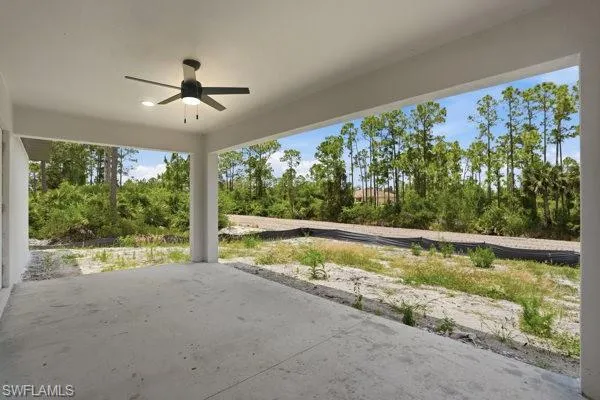 Covered patio with a ceiling fan, concrete flooring, and surrounding natural landscaping