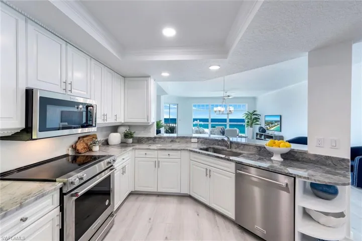 Kitchen featuring stainless steel appliances, a sink, a tray ceiling, crown molding, and a chandelier