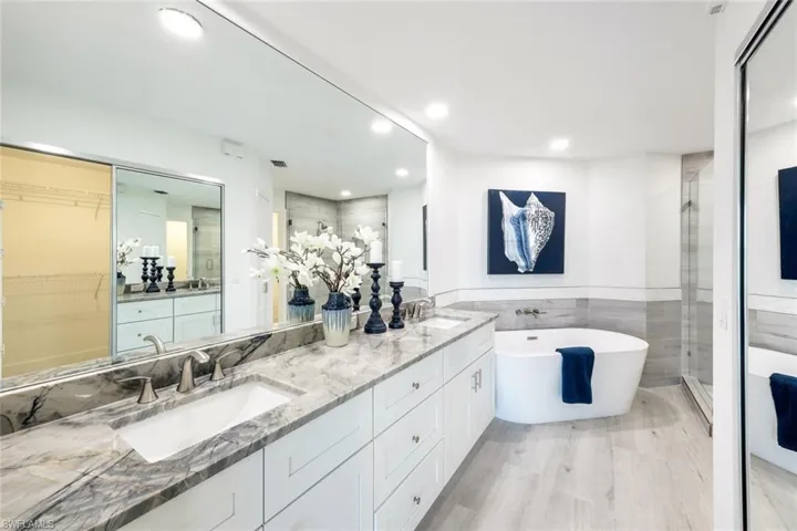 Full bath featuring a shower stall, a freestanding bath, double vanity, tile walls, and recessed lighting