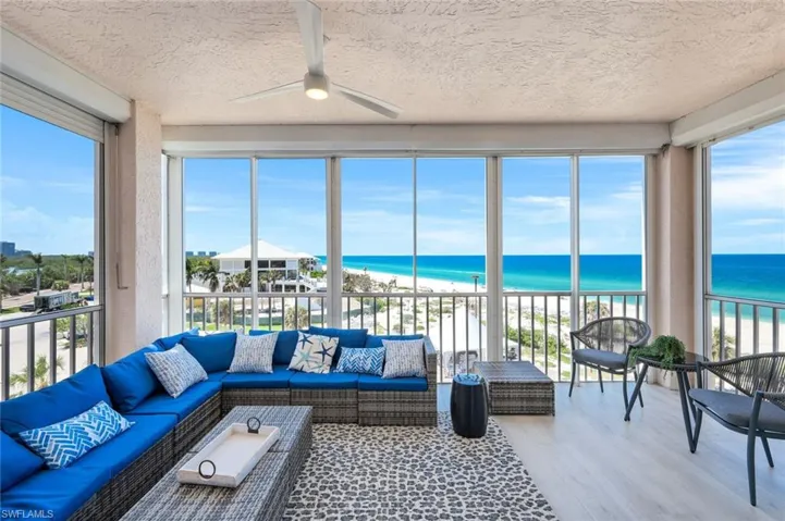 Sunroom with view of water and beach, wood finished floors, a textured ceiling, and healthy amount of natural light