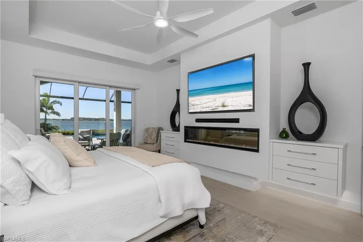 Primary suite is spacious and includes custom details: remote blackout shades on slider and windows, built-in California Closets in his/hers closets, built-in feature wall with custom drawers, entertainment center, electric fireplace, Troposair Titan ceiling fan, and the most amazing lake views.
