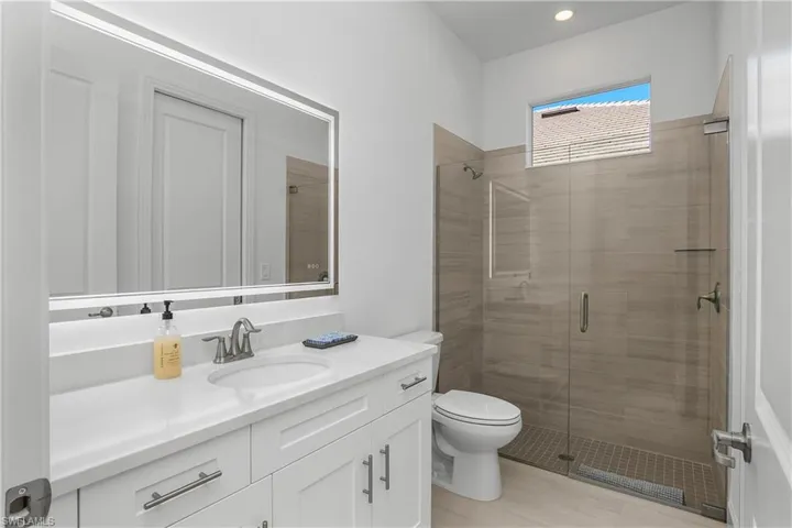 Full guest bath features frameless walk-in shower and custom backlit mirror.