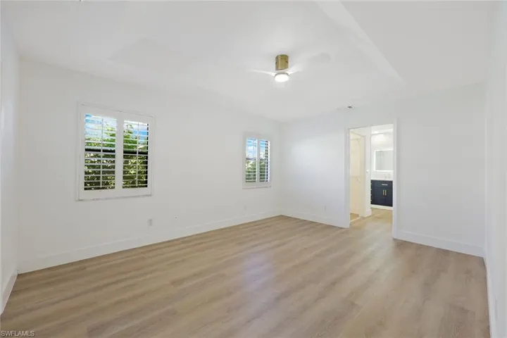 Primary Bedroom featuring a tray ceiling, a chandelier, light wood-style floors and French Doors leading to the pool area.