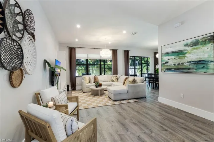 Recessed lighting illuminates the open living area featuring wood-finish flooring, a contemporary chandelier, and large windows with dark trim