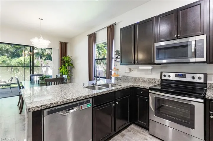 Kitchen featuring dark wood cabinetry, stainless steel appliances, granite countertops, and wood-finish flooring