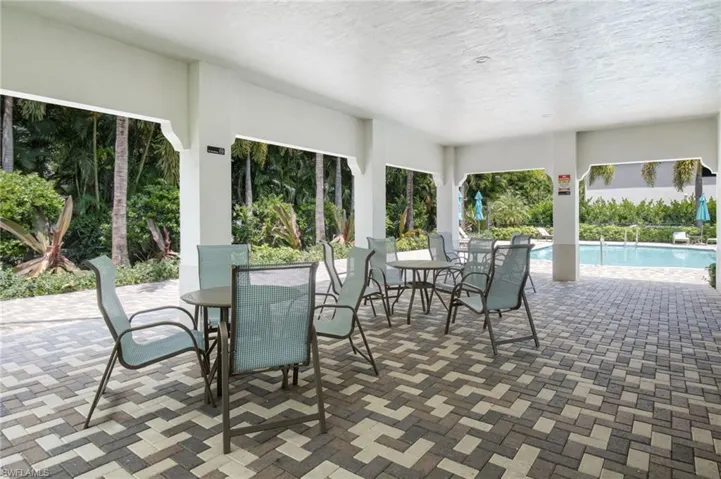 Covered outdoor patio with a patterned paver floor, columns, and an adjacent swimming pool