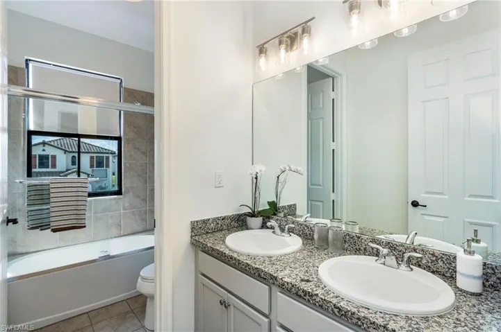 Double vanity with granite countertop and dual undermount sinks, complemented by a full-width mirror and a multi-bulb vanity light fixture