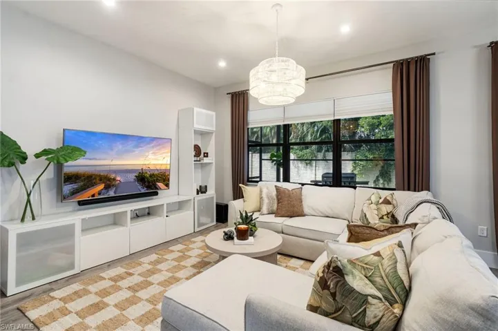 Recessed lighting, wood-finish flooring, built-in media console with open and closed storage, large picture windows, and a decorative pendant light