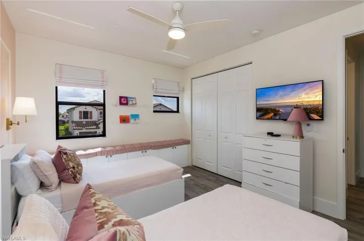 White ceiling fan, dual windows with custom blinds, built-in window seating with storage, double bi-fold closet, and wall-mounted television