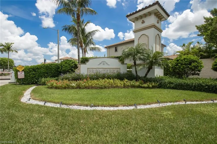Entryway featuring a decorative tower with arched accents, lush landscaping, and a stone-finish sign