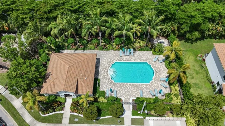 Gated community featuring a pool with a decorative surround, lush landscaping, and a tile roof