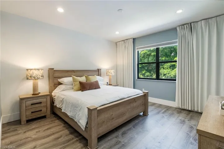 Wood-finish flooring, recessed ceiling lighting, light-toned walls, and a large window with white window treatments