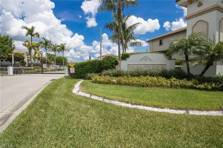 Gated community entrance featuring a stone-clad sign, lush landscaping, and mature palm trees