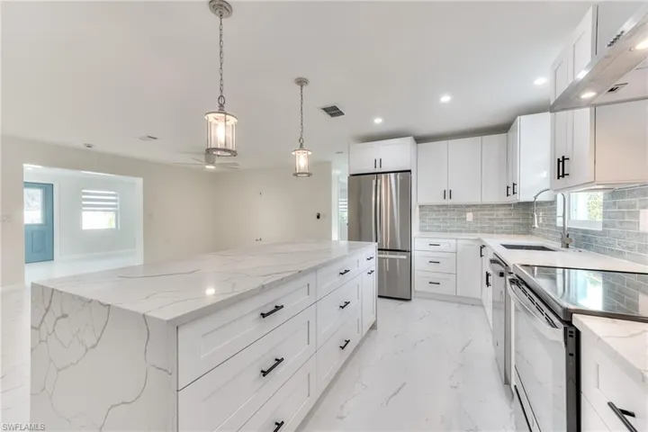 Kitchen with sink, white cabinetry, light stone countertops, a kitchen island, and stainless steel appliances