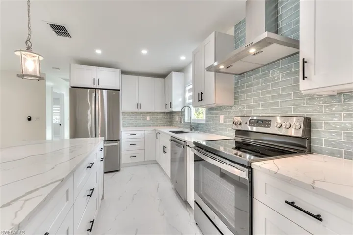 Kitchen featuring appliances with stainless steel finishes, white cabinetry, sink, light stone counters, and wall chimney exhaust hood