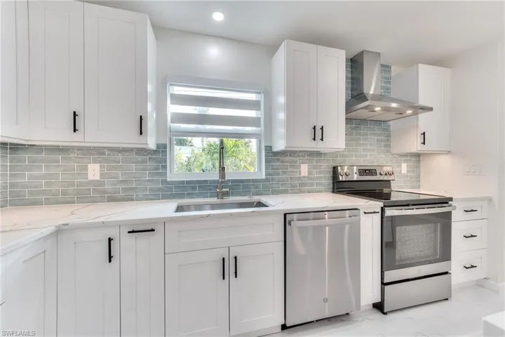 Kitchen with white cabinets, appliances with stainless steel finishes, wall chimney exhaust hood, tasteful backsplash, and sink