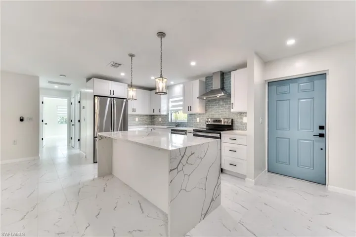 Kitchen featuring hanging light fixtures, white cabinets, a kitchen island, stainless steel appliances, and wall chimney exhaust hood