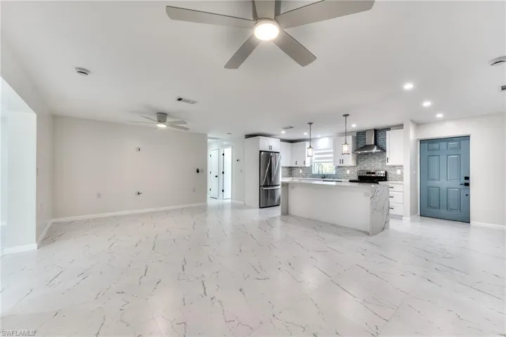 Kitchen featuring pendant lighting, wall chimney exhaust hood, white cabinetry, a kitchen island, and stainless steel appliances