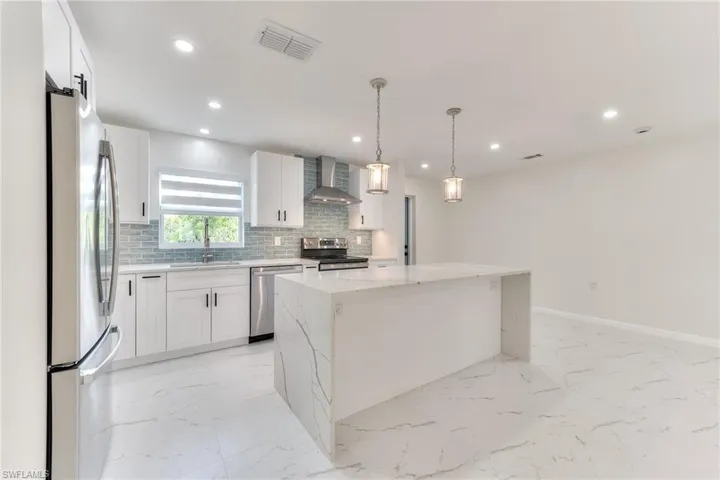Kitchen featuring appliances with stainless steel finishes, sink, white cabinets, wall chimney range hood, and a kitchen island