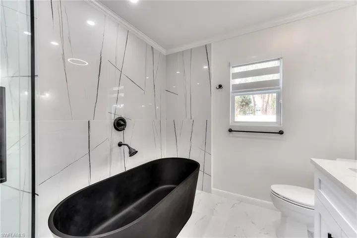 Bathroom featuring crown molding, toilet, vanity, and a bathtub
