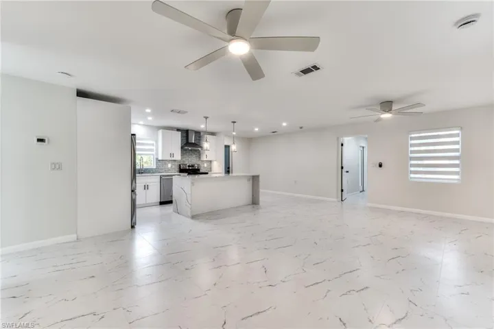 Kitchen with a center island, appliances with stainless steel finishes, white cabinetry, hanging light fixtures, and wall chimney range hood