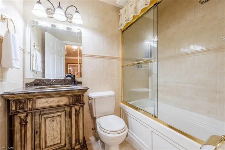 Full bathroom featuring tile walls, vanity, and bath / shower combo with glass door