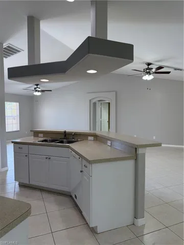 Kitchen featuring ceiling fan, a kitchen island with sink, open floor plan, light tile patterned flooring, and light countertops