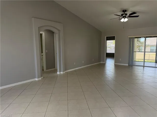 Empty room featuring a ceiling fan, vaulted ceiling, light tile patterned floors, and arched walkways