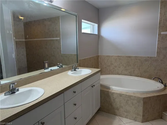Full bath with a garden tub, double vanity, light tile patterned floors, and a tile shower