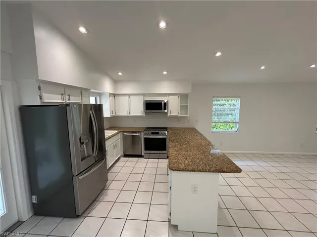 Kitchen featuring stainless steel appliances, white cabinetry, recessed lighting, light tile patterned floors, and dark stone countertops