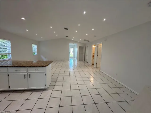 Kitchen with white cabinets, light tile patterned floors, open floor plan, vaulted ceiling, and dark stone counters