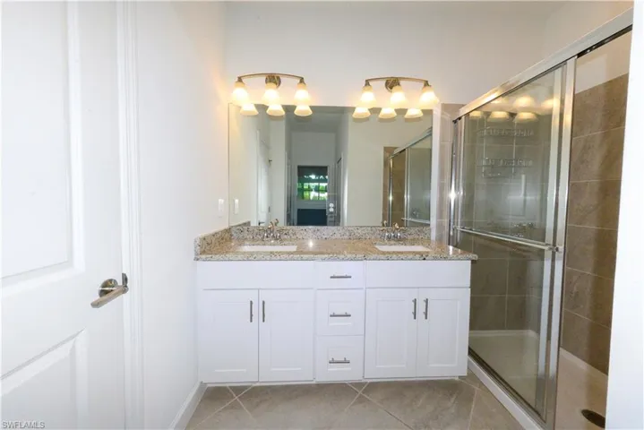 Full bath with double vanity, a shower stall, and light tile patterned floors