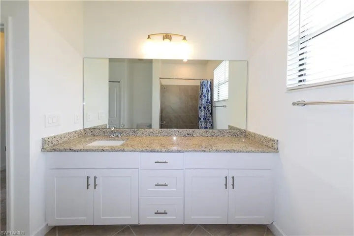 Full bath featuring double vanity, dark tile patterned flooring, and a tile shower