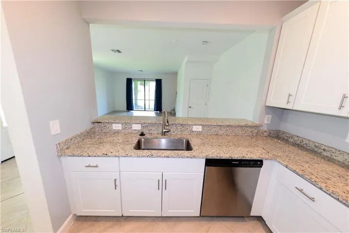 Kitchen featuring white cabinetry, dishwasher, light stone countertops, light tile patterned flooring, and a peninsula